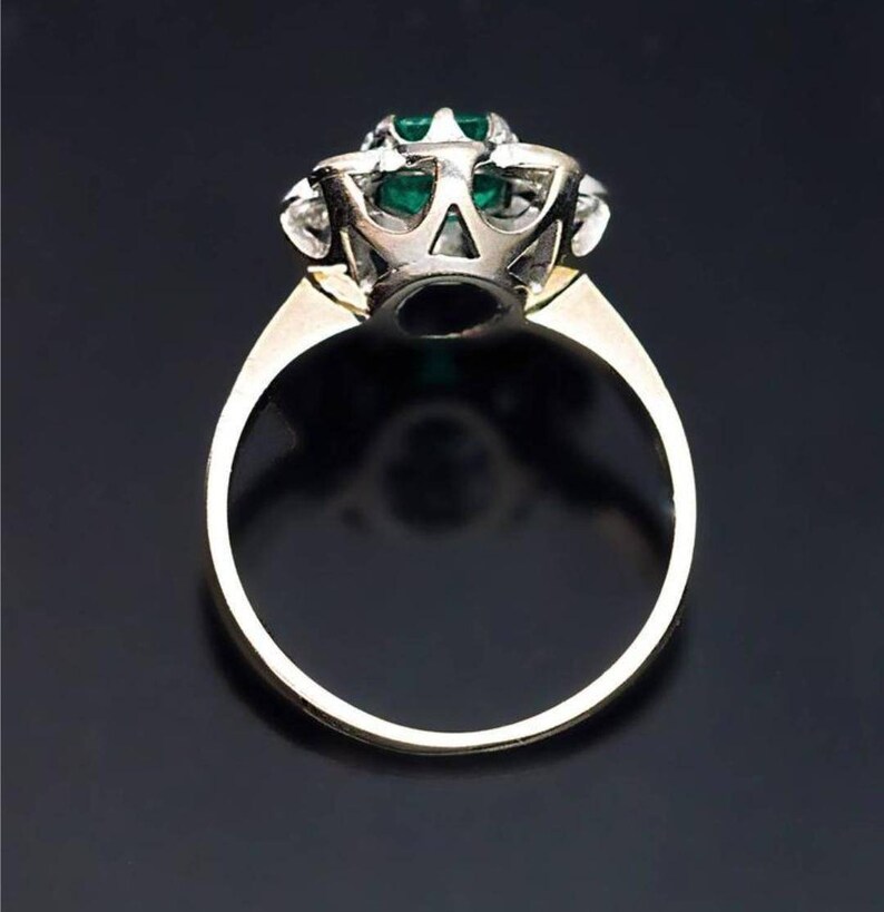 May include: A gold ring with a large emerald gemstone surrounded by smaller diamonds. The ring is set in a white metal setting.