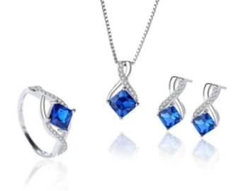 May include: A silver necklace, ring, and earrings set with a blue square gemstone and clear accents.