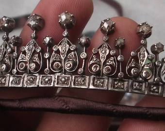 Könnte beinhalten: Eine silberne Tiara mit einem filigranen Design und kleinen, klaren Steinen. Die Tiara ist mit einer Reihe quadratischer Akzente verziert.