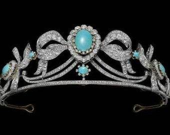 Puede incluir: Una tiara de plata con una piedra preciosa turquesa en el centro y piedras turquesas más pequeñas a los lados. La tiara está decorada con detalles intrincados y está engastada con diamantes.