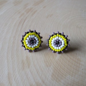 May include: A pair of beaded earrings with a circular design. The earrings are made with black, white, and yellow beads.
