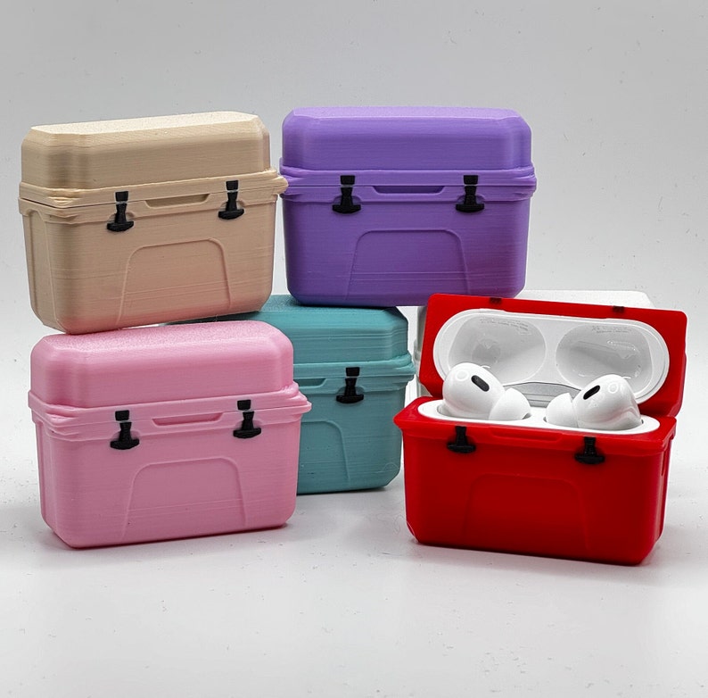 May include: A collection of colorful, miniature cooler-shaped cases for wireless earbuds. The cases are in various pastel colors, including pink, teal, purple, and beige. One red case is open, revealing white earbuds inside. Each case has a black latch.
