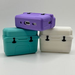 May include: Three small, rectangular, plastic containers in shades of purple, teal, and white. Each container has a hinged lid, black latches, and a textured surface. The purple container has a port on the side. The containers are stacked on top of each other.