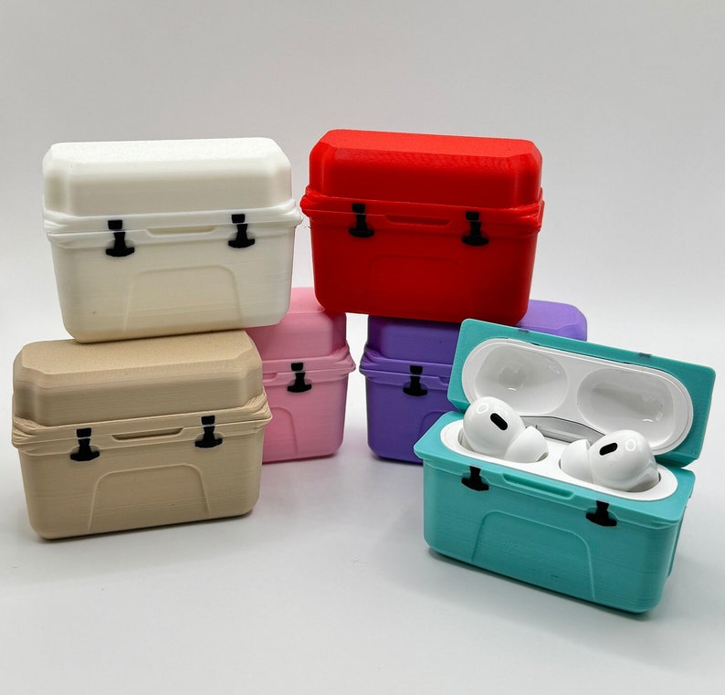 May include: A collection of colorful, miniature cooler-shaped cases for wireless earbuds. The cases are in various colors, including white, red, pink, purple, tan, and teal. One teal case is open, displaying white earbuds.