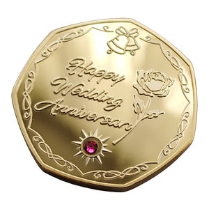 May include: Gold-toned octagonal coin with a pink gem in the centre. The coin features an engraved design with a rose, bells, and the text "Happy Wedding Anniversary".