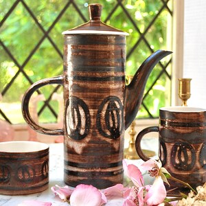 May include: A brown and white ceramic coffee pot, creamer, and sugar bowl set with a geometric pattern. The set has a rustic, vintage look.