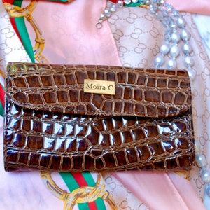 May include: A brown crocodile-embossed leather wallet with a gold metal plate that reads "Moira C".