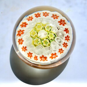 May include: A white glass paperweight with a swirling pattern of white, green, and orange flowers.