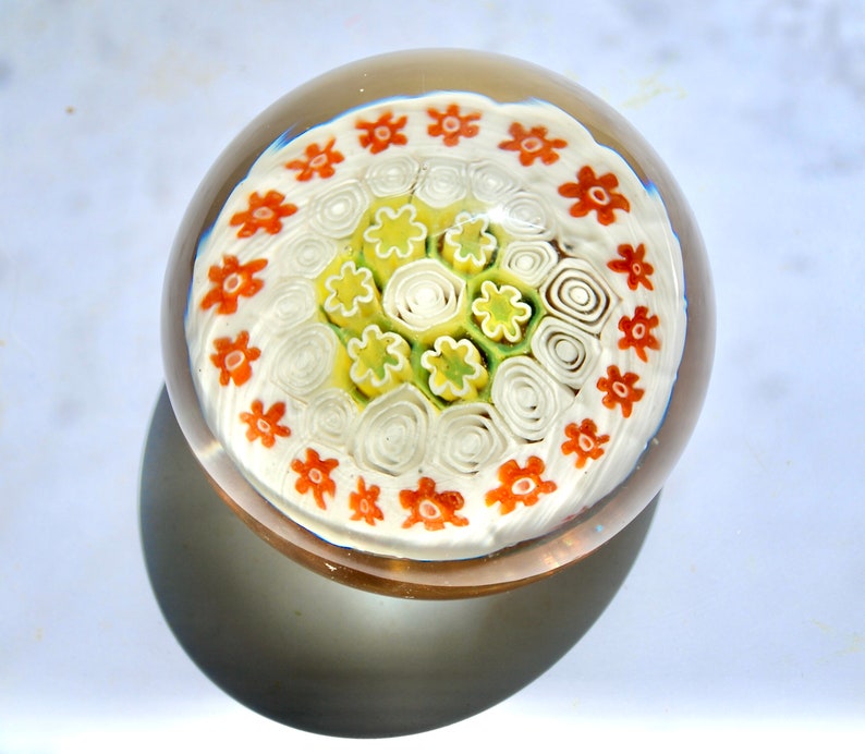 May include: A white glass paperweight with a swirling pattern of white, green, and orange flowers.