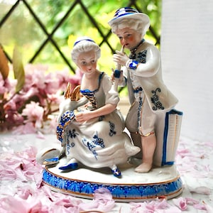 Porcelaine continentale vintage représentant une jeune bergère assise sur un manteau avec son amoureux jouant de la flûte, peint à la main en or et bleu