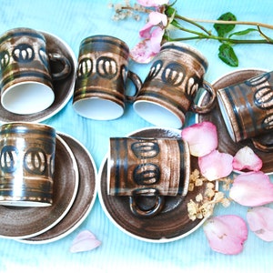 Puede incluir: Juego de seis tazas de café de cerámica marrón y negro con platillos a juego. Cada taza y platillo presenta un patrón geométrico.