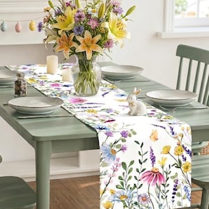 May include: A dining table set for a spring meal. The table is set with plates, a floral runner, and a vase of flowers. Green chairs surround the table. A decorative bunny figurine sits on the table runner.