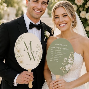 Pode incluir: Dois leques de casamento ovais com cabos de madeira. Um é creme com as letras M e W e a data 08.08.2026. O outro é verde sálvia com o texto PROGRAM SCHEDULE e uma lista de eventos de casamento, ambos com ilustrações florais.