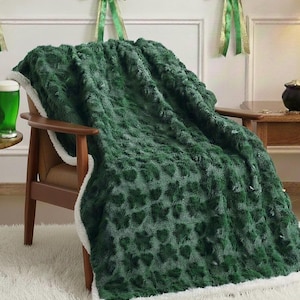 Puede incluir: Una manta verde con estampado de tréboles y borde blanco y esponjoso está sobre un sillón de madera. La manta tiene un aspecto texturizado. La silla está colocada contra una pared blanca con decoraciones de cintas verdes y doradas.