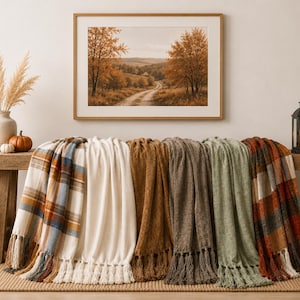 May include: A collection of six folded throw blankets draped over a wooden bench. The blankets feature various textures and patterns, including plaid designs in blue, orange, and brown, a solid cream color, and solid shades of brown, green, and rust.