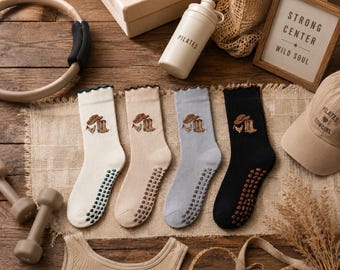 Puede incluir: Cuatro pares de calcetines antideslizantes de media caña en crema, beige, gris claro y negro. Cada calcetín tiene un borde superior con volantes y un diseño bordado de sombrero de vaquero, pañuelo y botas. Las suelas tienen puntos de agarre.
