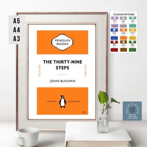 May include: A framed print of a book cover for "The Thirty-Nine Steps" by John Buchan. The cover is orange with a black penguin logo and the title in black text. The words "Fiction" are on either side of the title. The bottom of the cover says "Complete" and "Unabridged" with a black penguin illustration.
