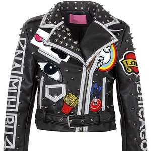 Op de afbeelding: Zwarte leren jas met zilveren studs en patches. Voorzien van een ritssluiting, riem en witte strepen. Patches: regenboog, oog, gitaar en teksten "CHICAGO" en "ZNA MIBIZ".