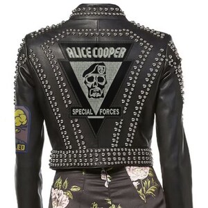 May include: Black leather jacket with silver stud embellishments. Features a triangular patch on the back with "ALICE COOPER" and "SPECIAL FORCES" text, along with a skull graphic. The jacket has a cropped design and long sleeves.