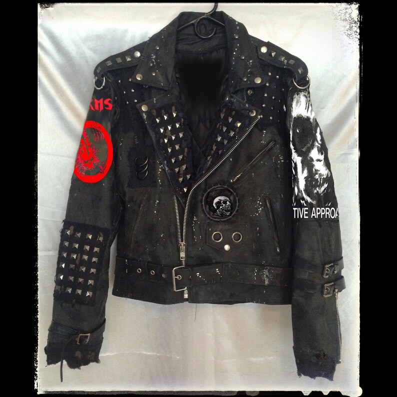 Puede incluir: Chaqueta de cuero negra adornada con tachuelas plateadas, parches y un dise&ntilde;o de calavera. La chaqueta tiene cierre de cremallera, m&uacute;ltiples hebillas y la palabra "KRIS" en el hombro izquierdo. La manga derecha tiene las palabras "TIVE APPROA" y un dise&ntilde;o de calavera.