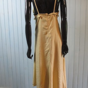 May include: A light beige sleeveless dress with a scoop neck and a gathered skirt. The dress has a simple design and is made of a lightweight fabric.