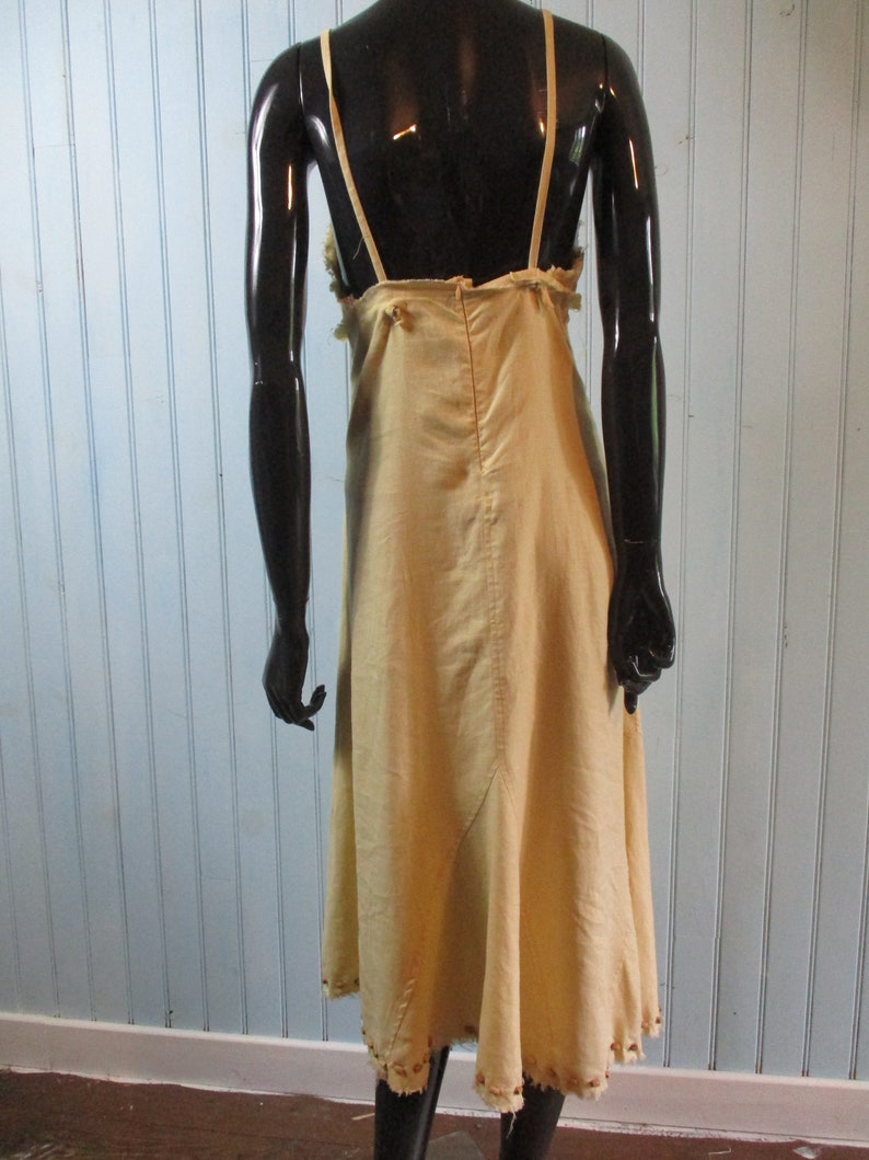 May include: A light beige sleeveless dress with a scoop neck and a gathered skirt. The dress has a simple design and is made of a lightweight fabric.