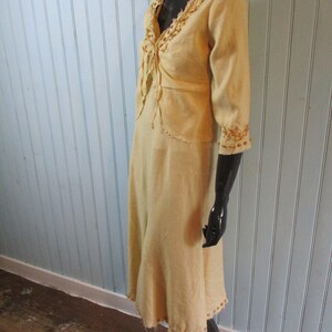 May include: A light yellow dress with a long skirt and a short-sleeved top. The dress has a V-neckline and is decorated with brown embroidery around the neckline and sleeves.