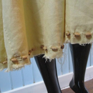 May include: A pale yellow linen skirt with a raw edge hem. The skirt is decorated with a row of wooden beads.