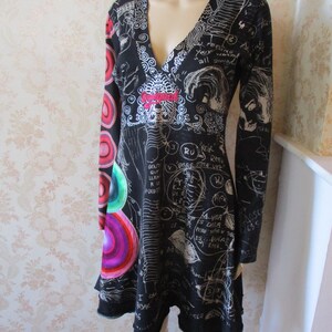 May include: Black long-sleeved dress with a V-neckline and a white print of scribbles and circles. The dress has a flared skirt and a red embroidered detail on the front.