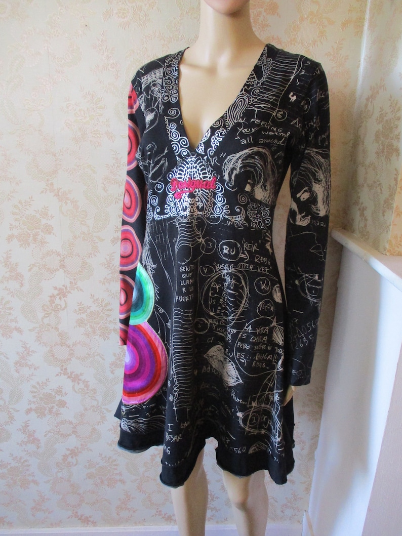 May include: Black long-sleeved dress with a V-neckline and a white print of scribbles and circles. The dress has a flared skirt and a red embroidered detail on the front.