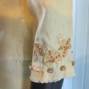 May include: A light yellow linen top with a frayed hem and embroidered leaf design with brown beads.