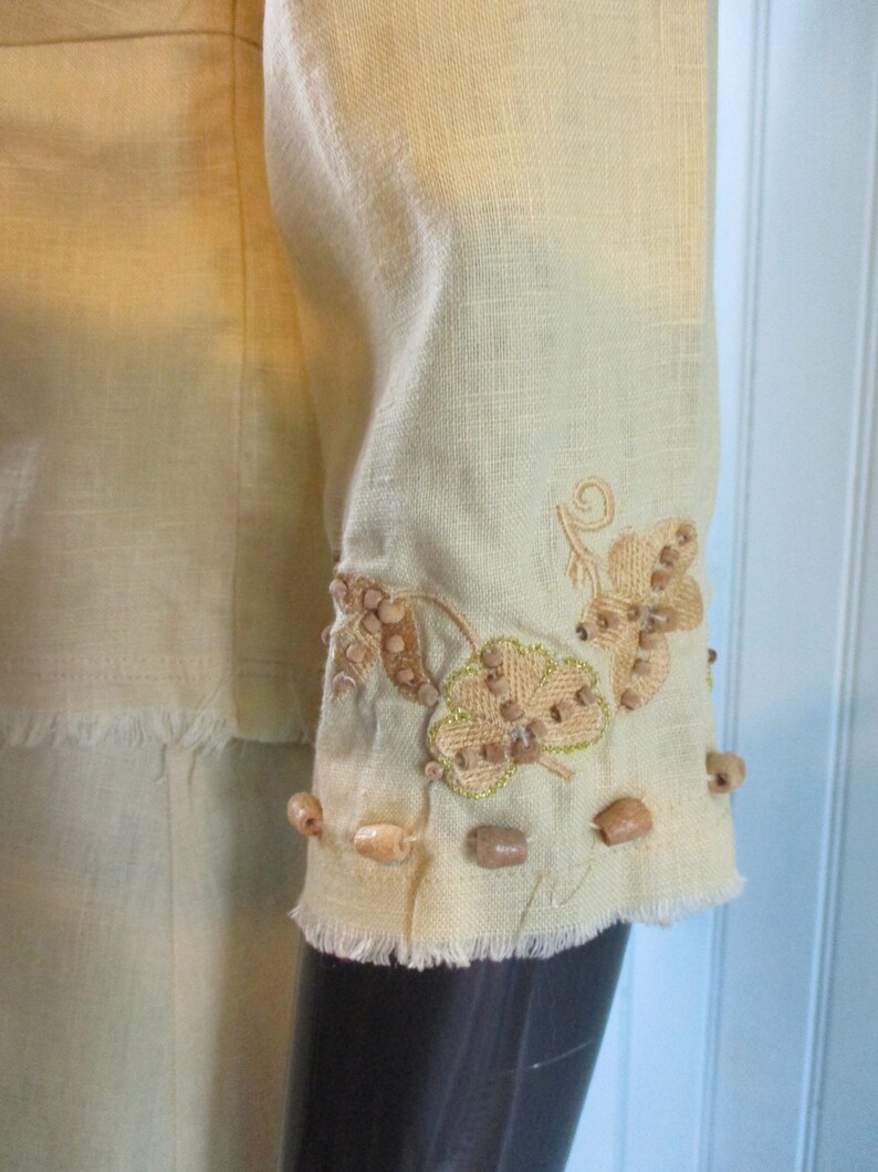 May include: A light yellow linen top with a frayed hem and embroidered leaf design with brown beads.