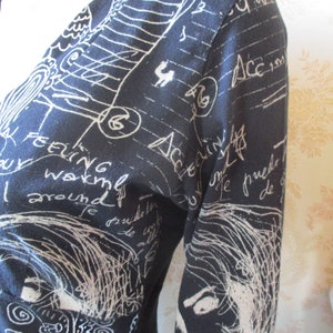 May include: A black long-sleeved dress with a white print of handwritten text and drawings. The text includes the words "feeling" and "around".