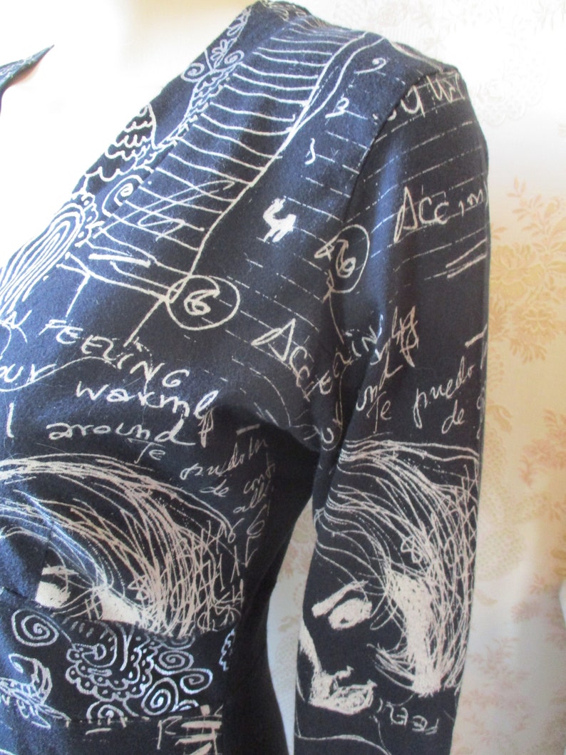 May include: A black long-sleeved dress with a white print of handwritten text and drawings. The text includes the words "feeling" and "around".