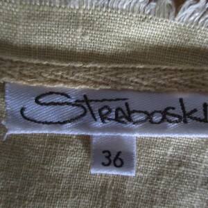 May include: A white tag with black text that reads "Strabovski" and a smaller white tag with the number "36" on a beige fabric background.