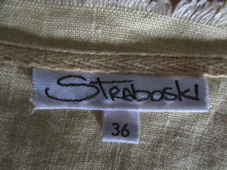 May include: A white tag with black text that reads "Strabovski" and a smaller white tag with the number "36" on a beige fabric background.