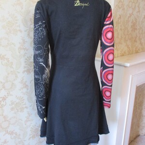 May include: Black long-sleeved dress with a white print on one sleeve and a colorful circle print on the other sleeve. The dress has a round neckline and the word "Desigual" is embroidered on the back.