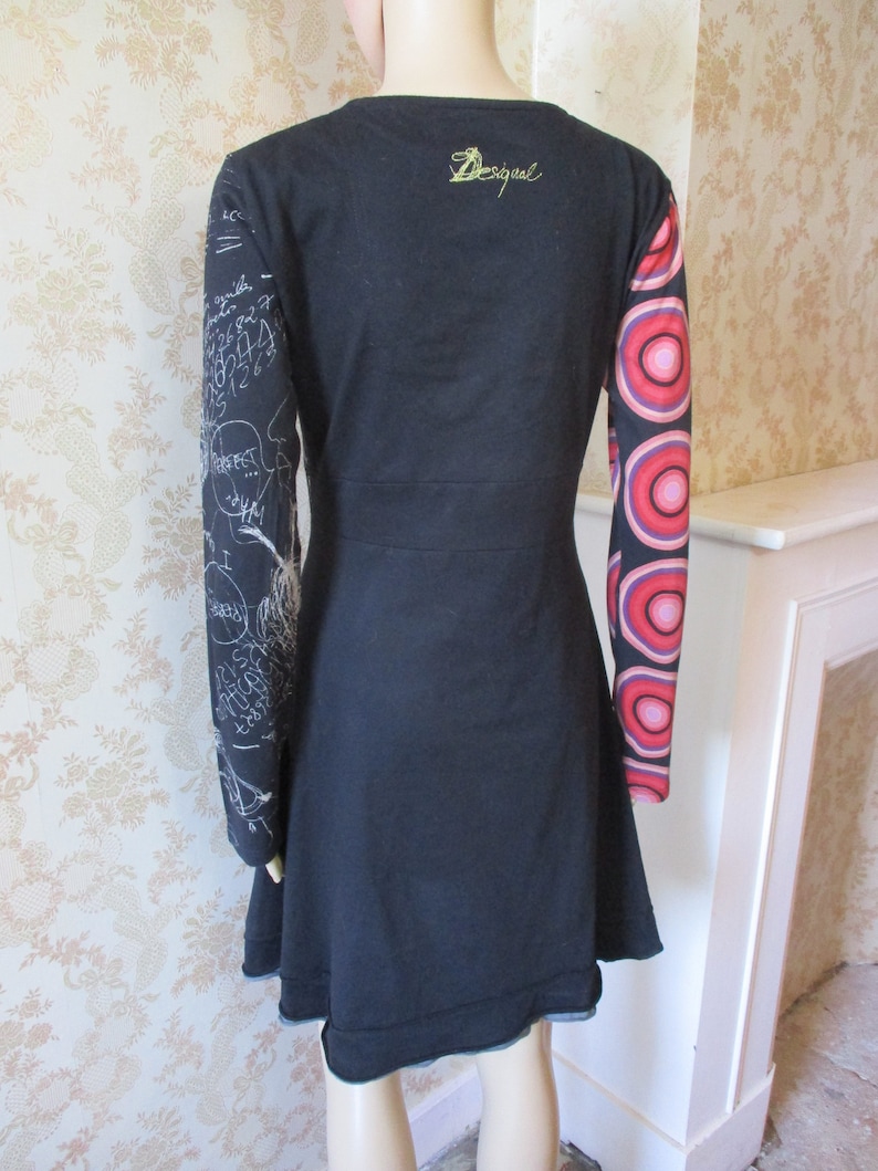 May include: Black long-sleeved dress with a white print on one sleeve and a colorful circle print on the other sleeve. The dress has a round neckline and the word "Desigual" is embroidered on the back.