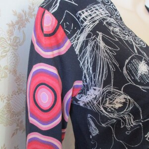May include: Black long-sleeved dress with a white abstract design and a colorful circular pattern on the sleeves.