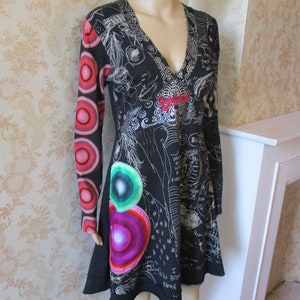 May include: Black long-sleeved dress with a V-neckline and a colorful abstract print. The dress has a fitted bodice and a flared skirt. The print includes circles, swirls, and scribbles.