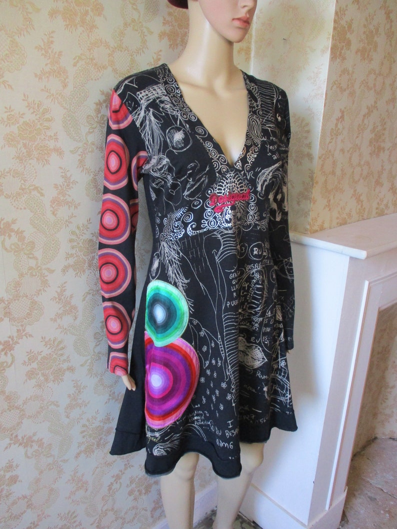 May include: Black long-sleeved dress with a V-neckline and a colorful abstract print. The dress has a fitted bodice and a flared skirt. The print includes circles, swirls, and scribbles.