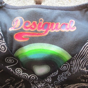 May include: Black and white patterned shirt with a v-neck and the word "Desigual" printed in gold and pink letters on the front.