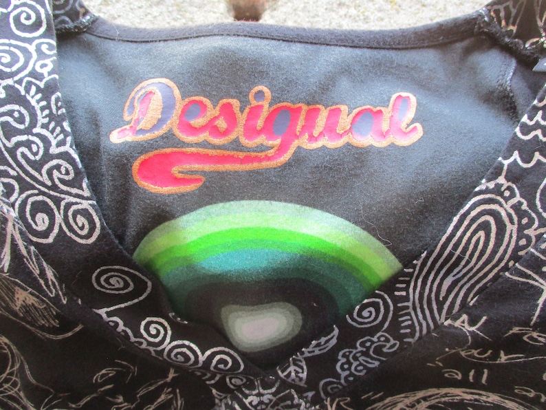 May include: Black and white patterned shirt with a v-neck and the word "Desigual" printed in gold and pink letters on the front.