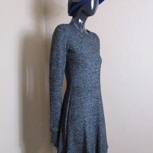 May include: A grey and black long-sleeved dress with a flared skirt. The dress is on a mannequin wearing a blue hat with a grey bow.
