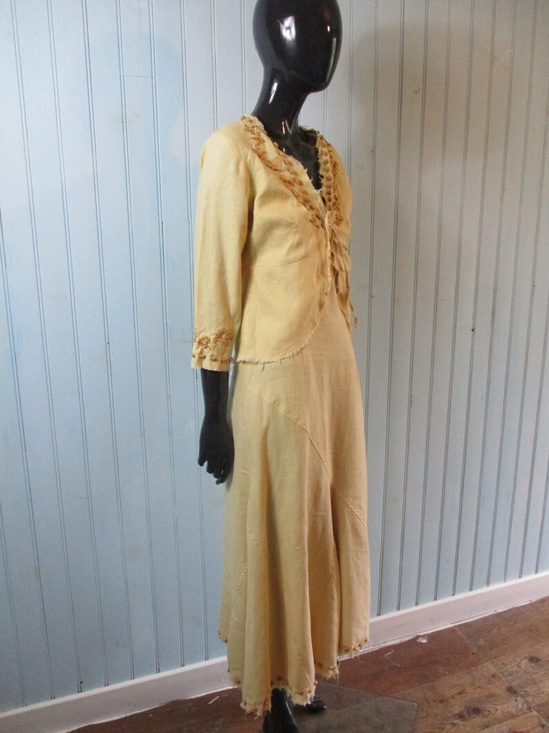 May include: A long, flowing dress in a pale yellow color with brown embroidery around the neckline and hem. The dress is made of a lightweight fabric and has a relaxed fit.