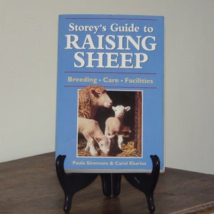May include: A blue book titled "Storey's Guide to Raising Sheep: Breeding, Care, Facilities" by Paula Simmons and Carol Ekarius. The cover features a photo of a sheep and two lambs.