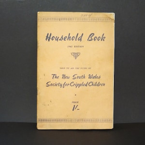 Könnte beinhalten: Ein beigefarbenes Buch mit dem Titel "Household Book" mit dem Jahr 1941 und den darunter gedruckten Worten "Edition". Das Buch wird verkauft, um die Mittel der "The New South Wales Society for Crippled Children" zu unterstützen. Der Preis ist mit "1/-." angegeben.