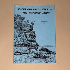 May include: A softcover book titled Rocks and Landscapes of the Sunshine Coast by W.F. Willmott and N.C. Stevens. The light blue cover features a black ink illustration of a rocky coastal cliffside with vegetation overlooking the ocean.