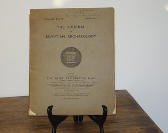 以下が含まれることがあります： ロンドンでThe Egypt Exploration Fundが出版した「The Journal of Egyptian Archaeology」Volume II、Part IVのヴィンテージブックカバー。表紙は色あせたタン色で、黒い文字と円形のエンブレムが特徴です。「1915年10月」の日付が見えます。
