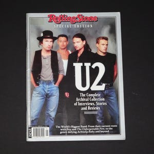 以下が含まれることがあります： ローリングストーン特別版マガジン、U2のバンドを特集。表紙にはバンドメンバーの集合写真が掲載されています。雑誌のタイトルとバンド名が大きく表示されています。表紙のテキストには「The Complete Archival Collection of Interviews, Stories and Reviews」と書かれています。